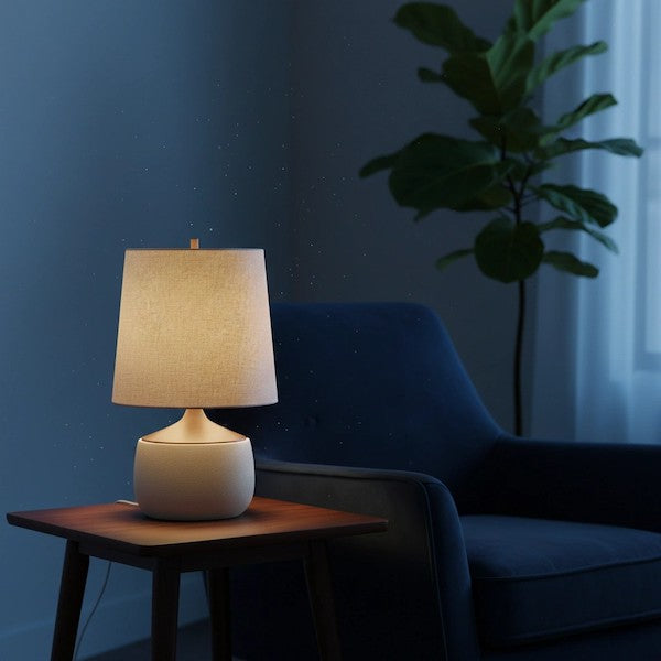 A cozy living room at sunset featuring a mid-century ceramic lamp providing a warm glow on a wooden side table.