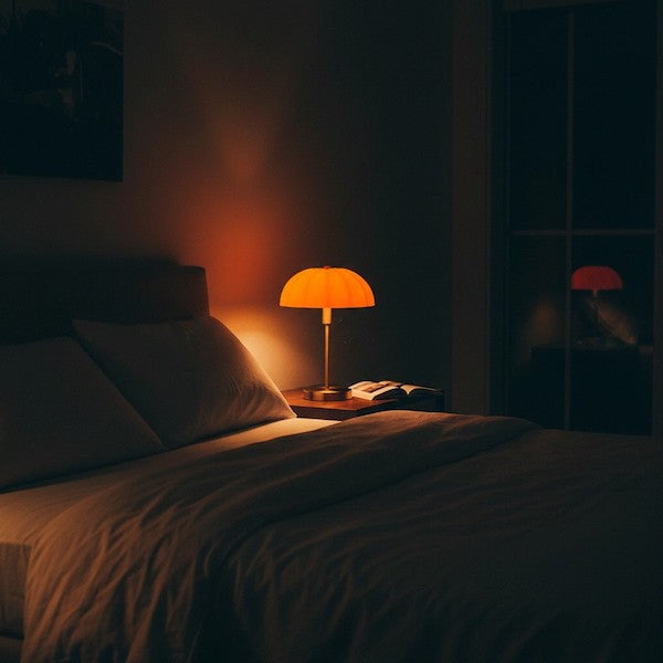 A cozy bedroom at night featuring the soft, orange glow of a pumpkin lamp on a nightstand.