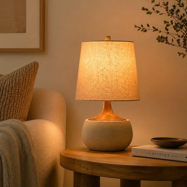 Mid-century modern accent lamp with cement base and linen shade glowing in a minimalist living room.